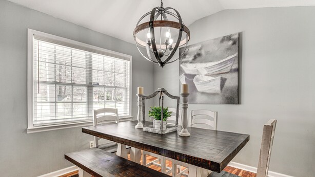 A dining area with a dark wooden table, white chairs, a chandelier, and a large window with blinds. - Lakefront Guntersville Base: Boat Parking & Power! (Scottsboro)