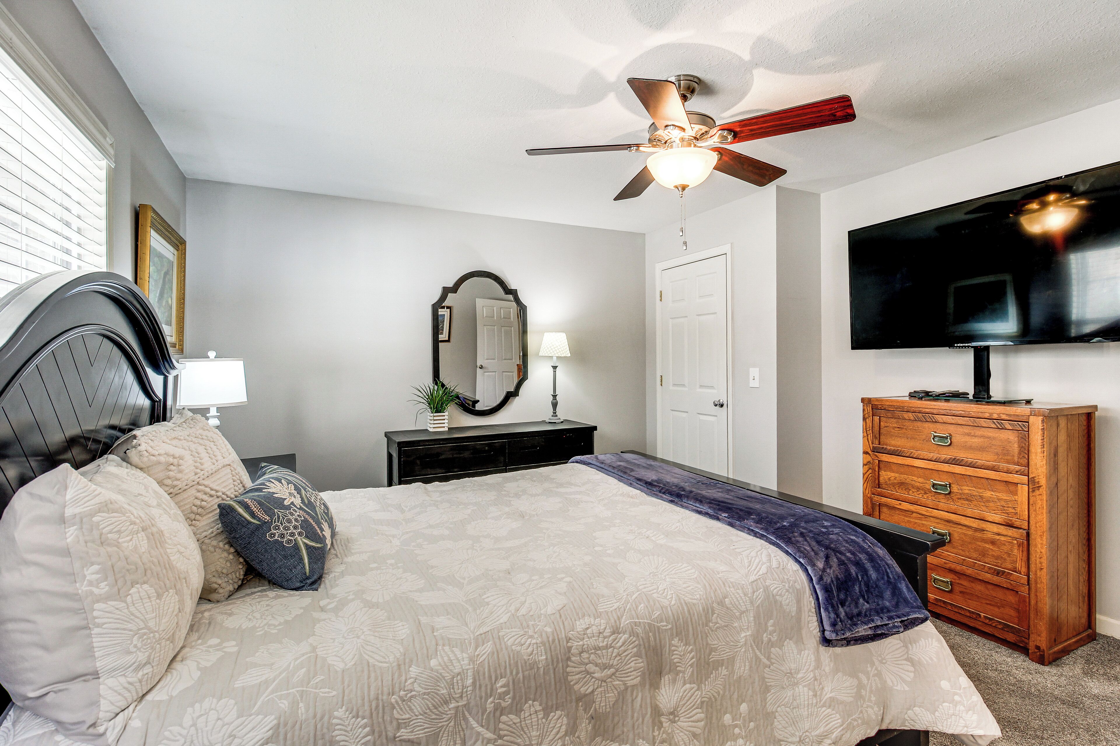 A bedroom with a bed, a dresser, a television, a ceiling fan, and a mirror.