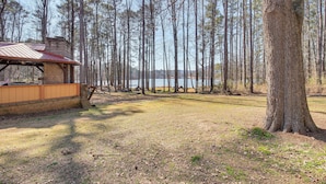 A rustic cabin with a metal roof and brick walls, surrounded by tall trees and a lake in the background. - Lakefront Guntersville Base: Boat Parking & Power! (Scottsboro)