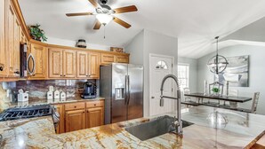A kitchen with wooden cabinets, stainless steel appliances, a marble countertop, and a ceiling fan. - Lakefront Guntersville Base: Boat Parking & Power! (Scottsboro)