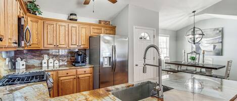 A kitchen with wooden cabinets, stainless steel appliances, a marble countertop, and a ceiling fan.