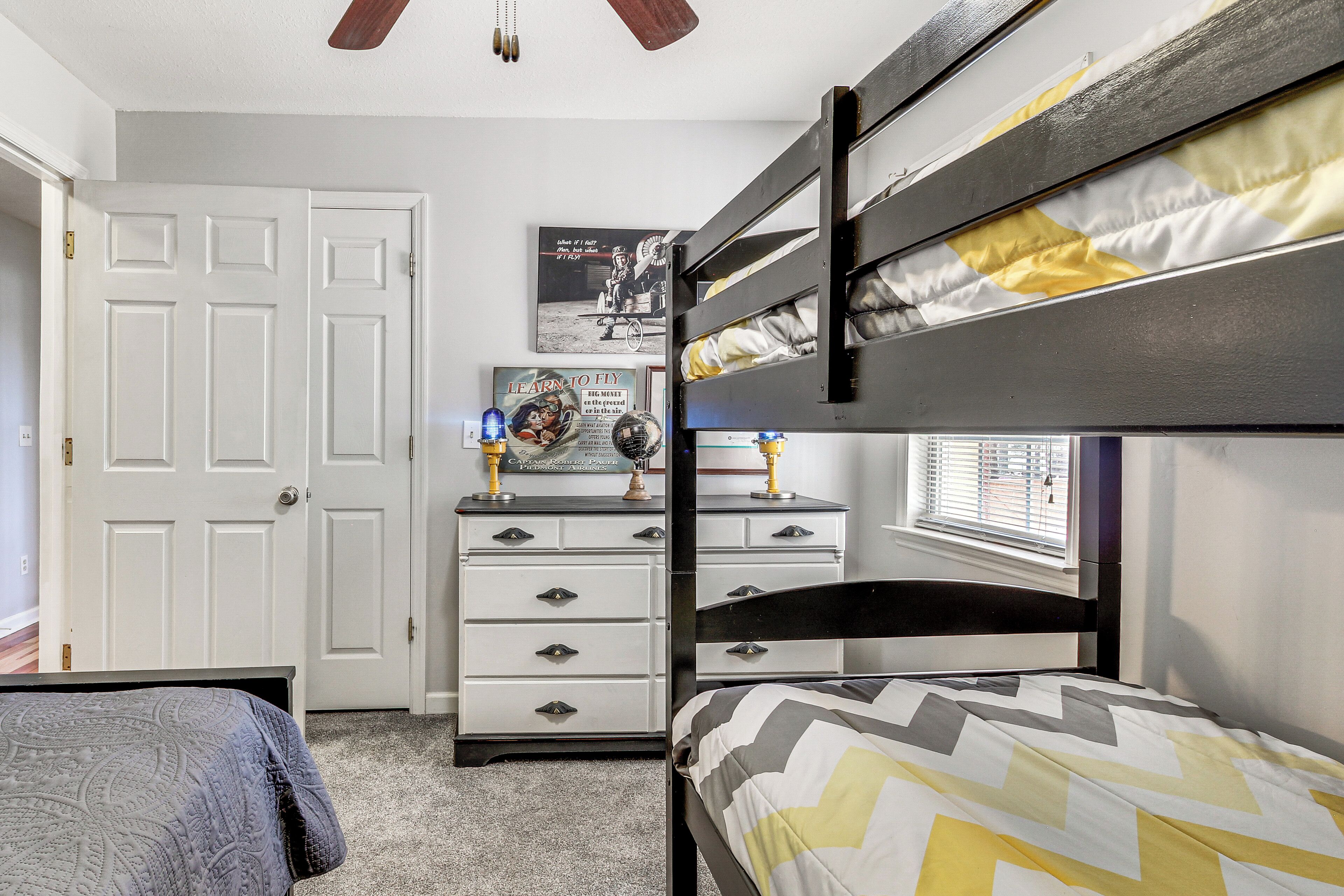 A bunk bed room with a dresser, a door, and a poster on the wall.