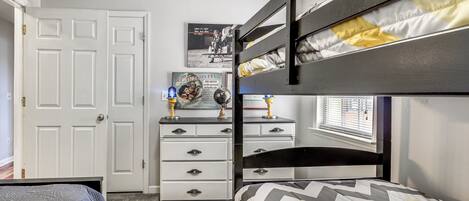 A bunk bed room with a dresser, a door, and a poster on the wall.