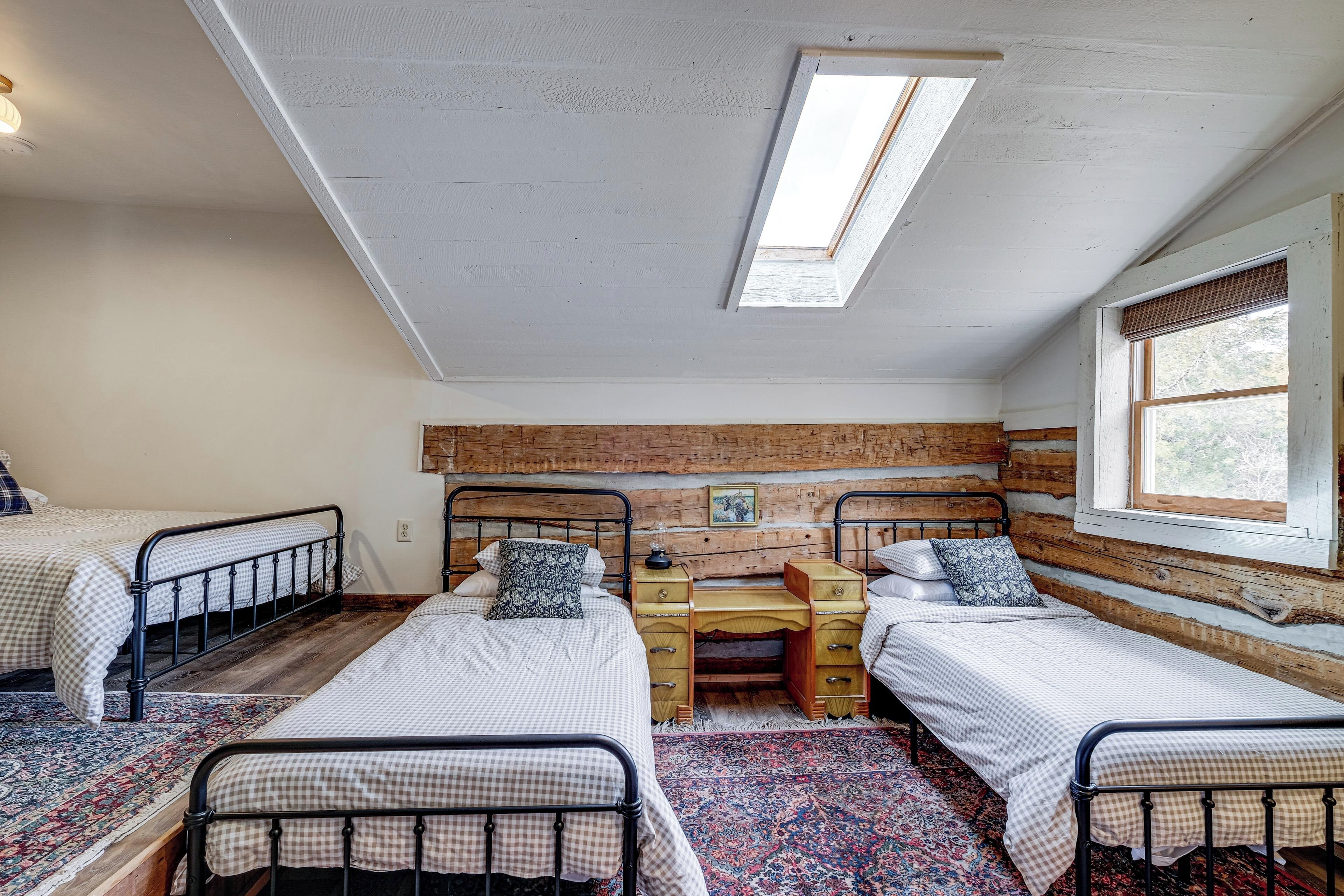 A room with three beds, a wooden desk, and a skylight.