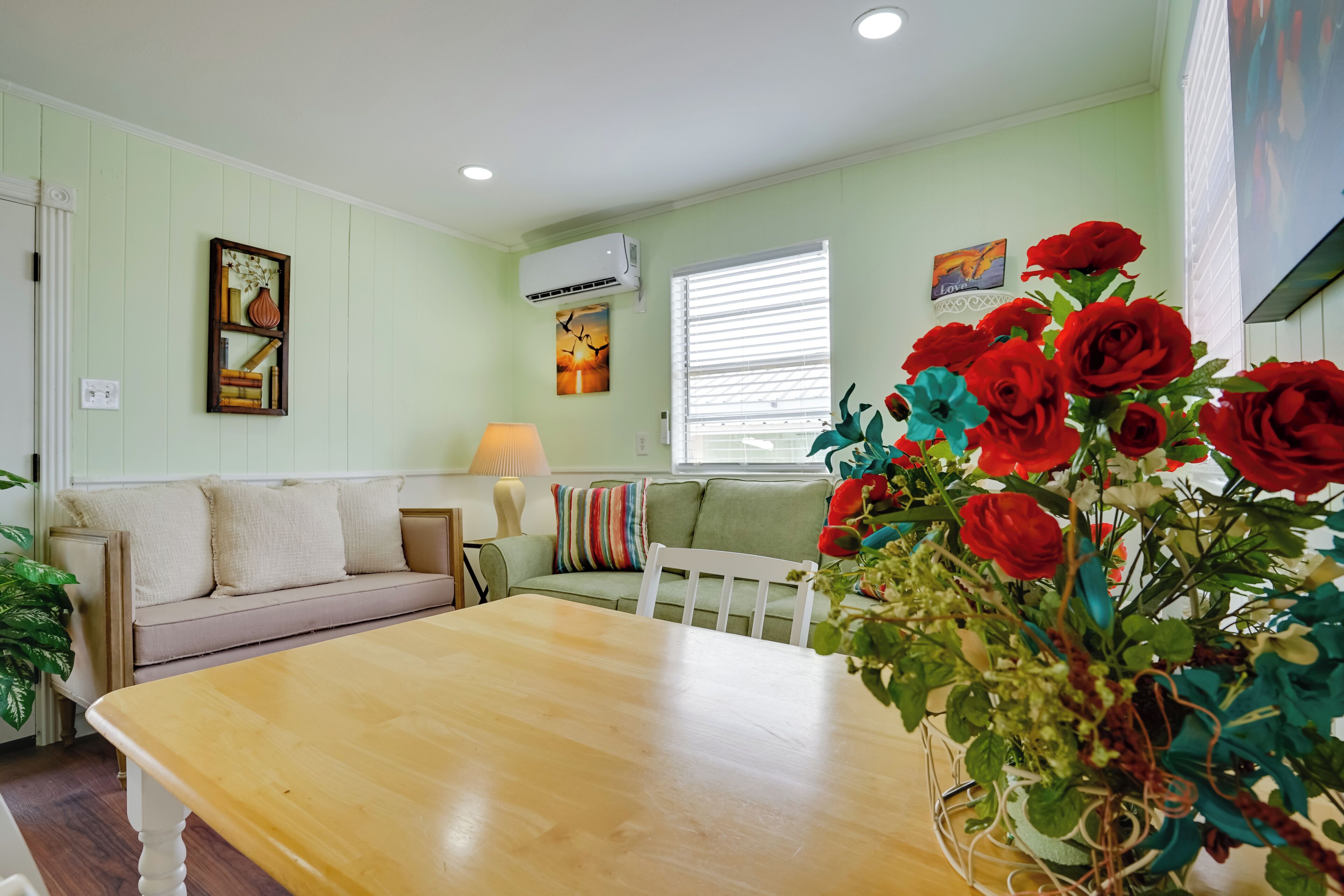 A living room with a wooden table, a green sofa, and a window with blinds.