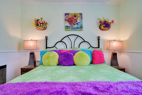 A bed with colorful pillows, two wall-mounted flower baskets, and a painting above the bed.