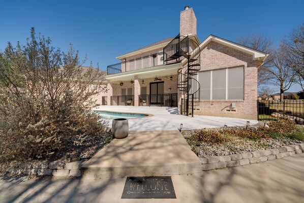 A two-story house with a balcony, a pool, and a welcome mat. - Near Joe Pool Lake! Luxe Getaway w/ Shared Pool (Cedar Hill)