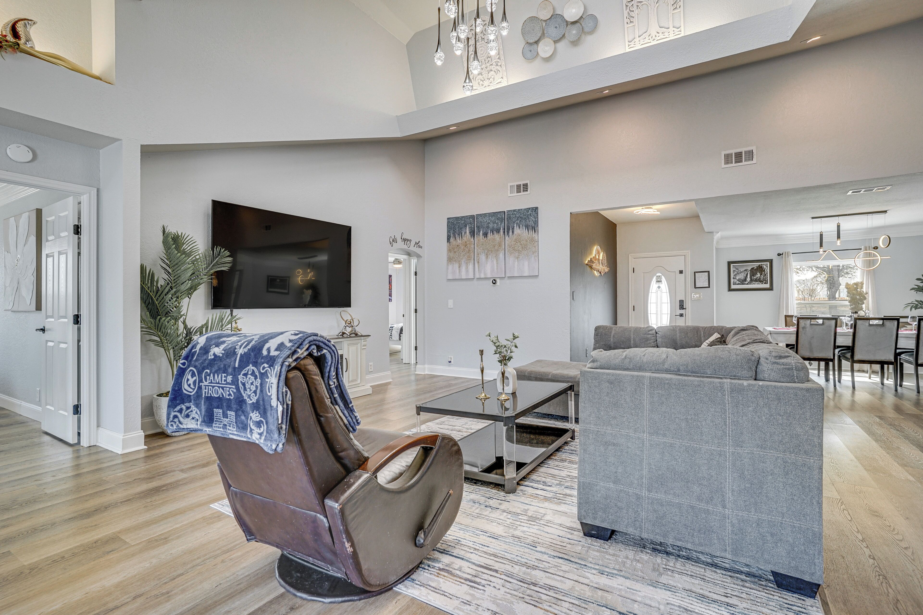A spacious living room with a leather armchair, a gray sofa, and a flat-screen TV mounted on the wall.