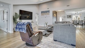 A spacious living room with a leather armchair, a gray sofa, and a flat-screen TV mounted on the wall. - Private 1-acre Hideaway, 2 Mi to Joe Pool Lake! (Grand Prairie)