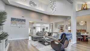 A spacious living room with a gray sofa, a leather chair, and a glass coffee table. There is a dining area with a table and chairs visible in the background. - Private 1-acre Hideaway, 2 Mi to Joe Pool Lake! (Grand Prairie)