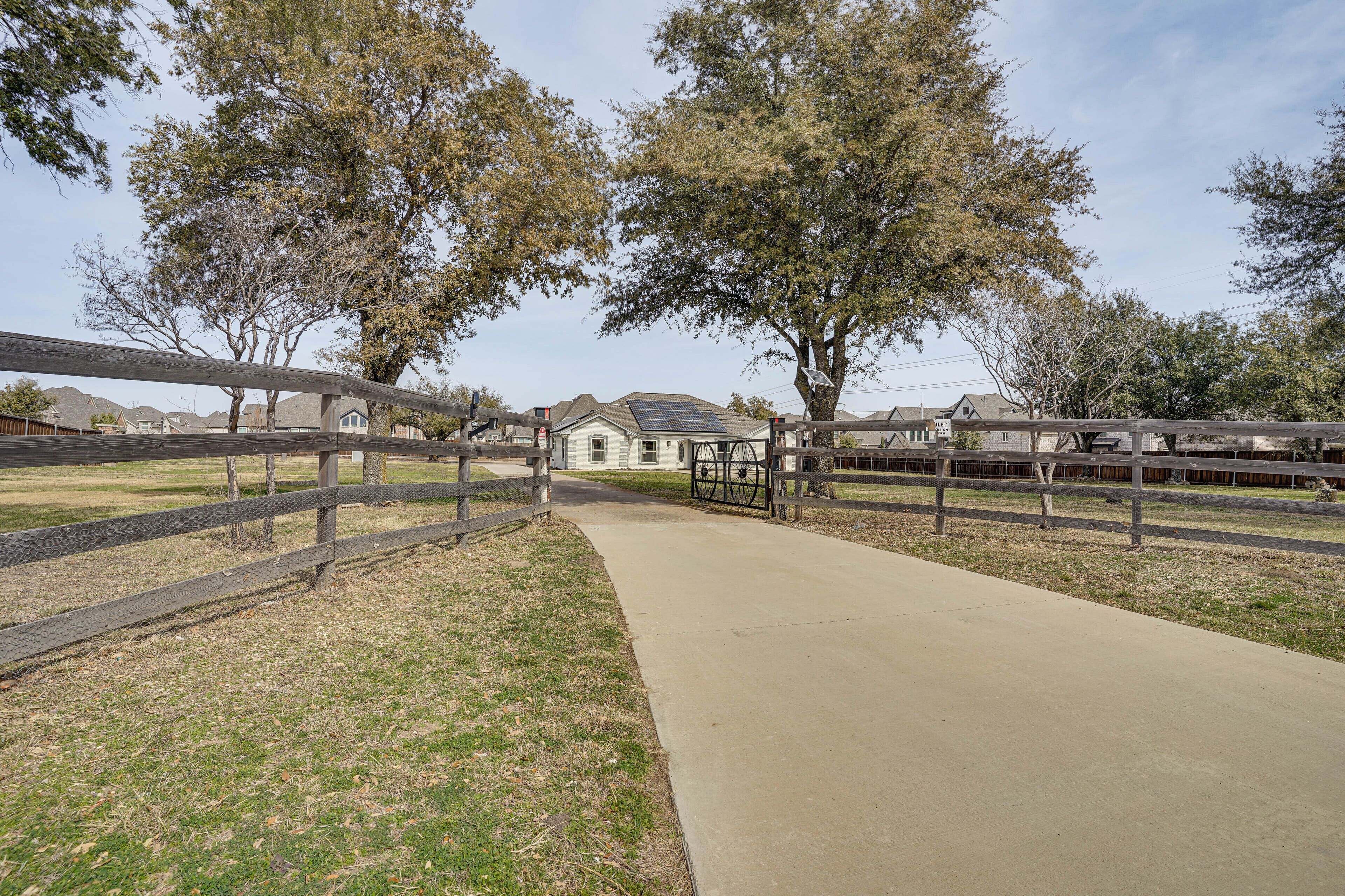 A pathway leading to a building with a solar panel, surrounded by trees and a wooden fence.