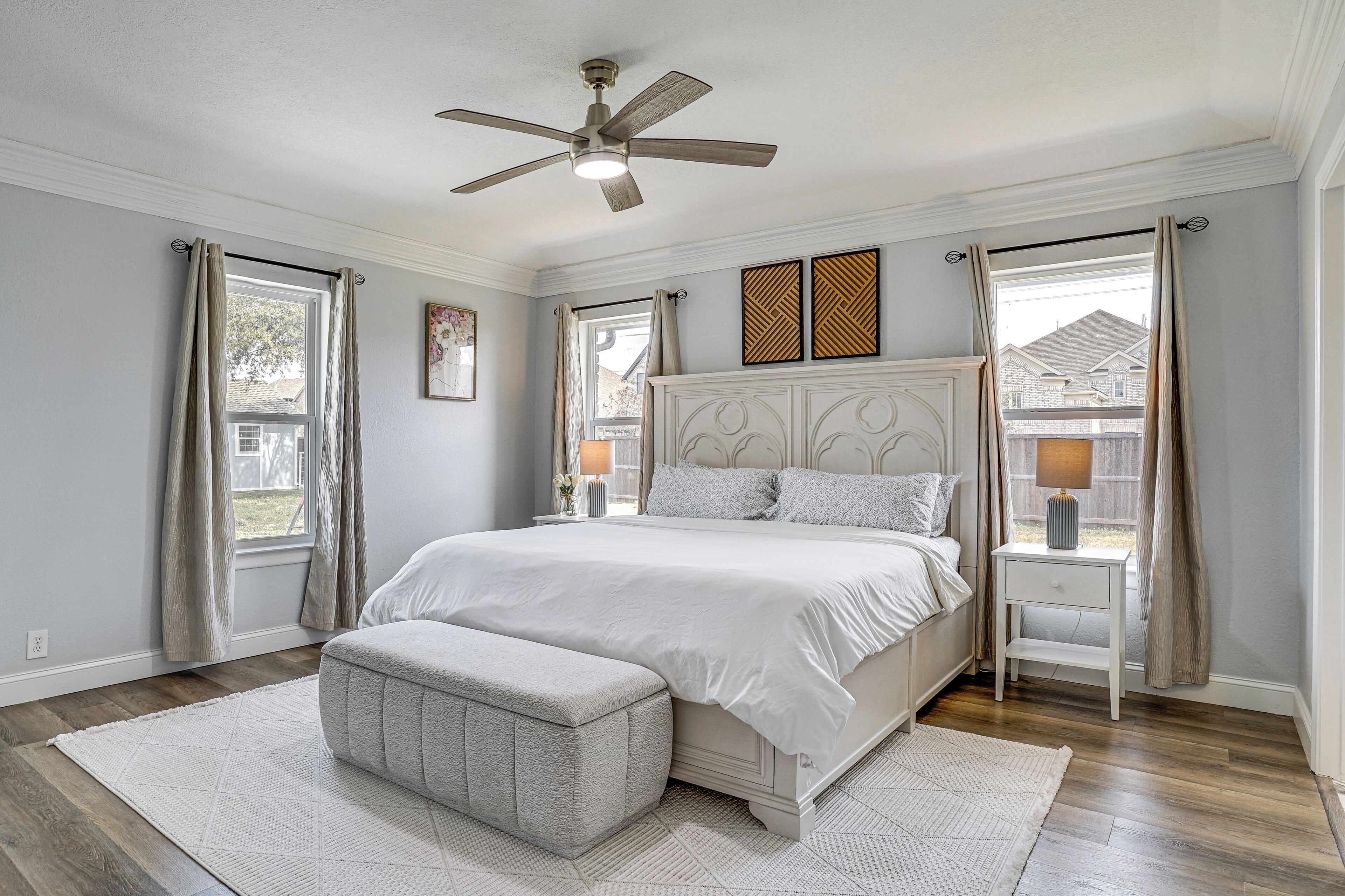 A bedroom with a bed, a nightstand, a bench, a ceiling fan, and a window with curtains.