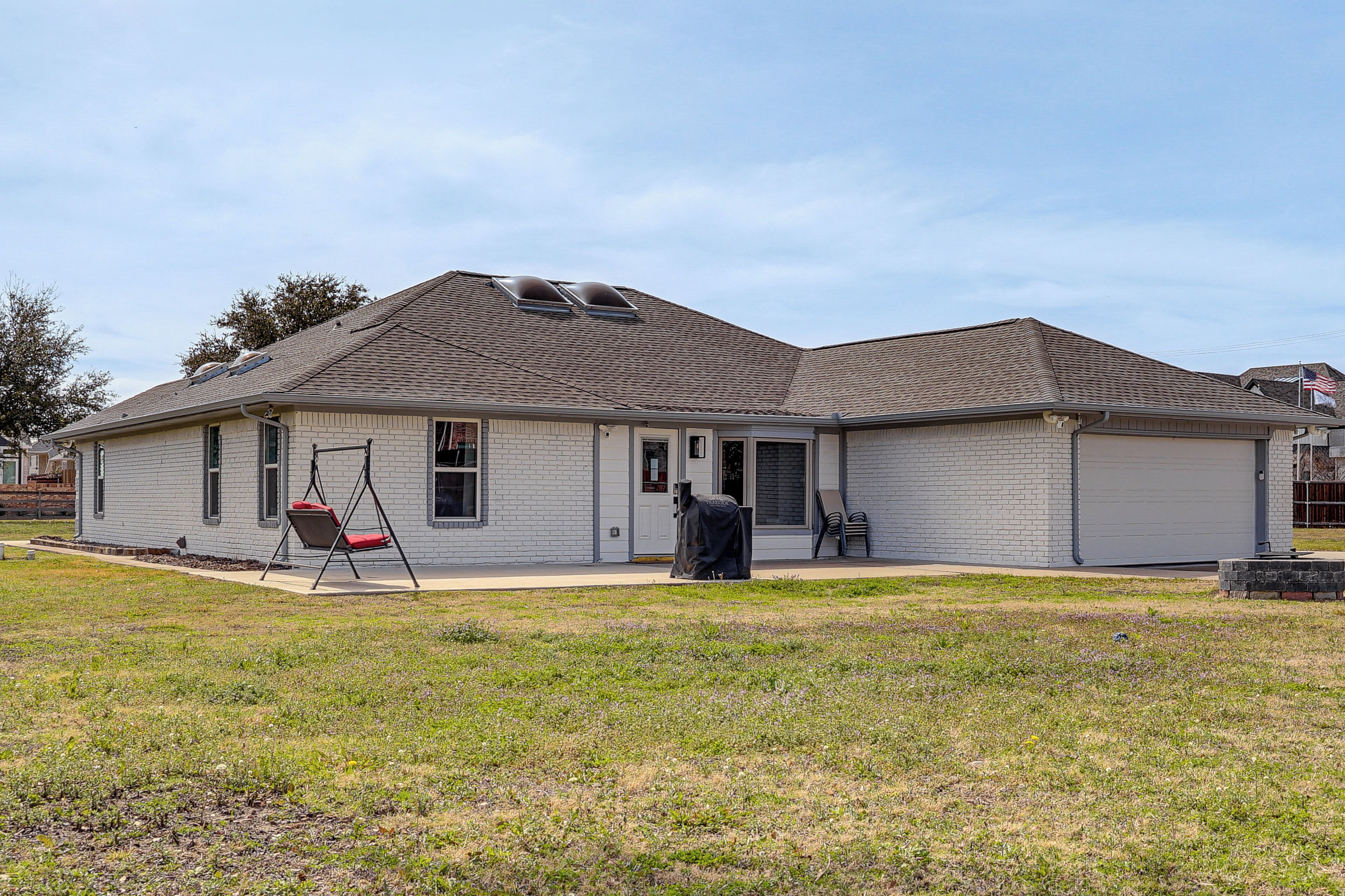 A single-story house with a covered patio, a swing set, and a covered grill area.