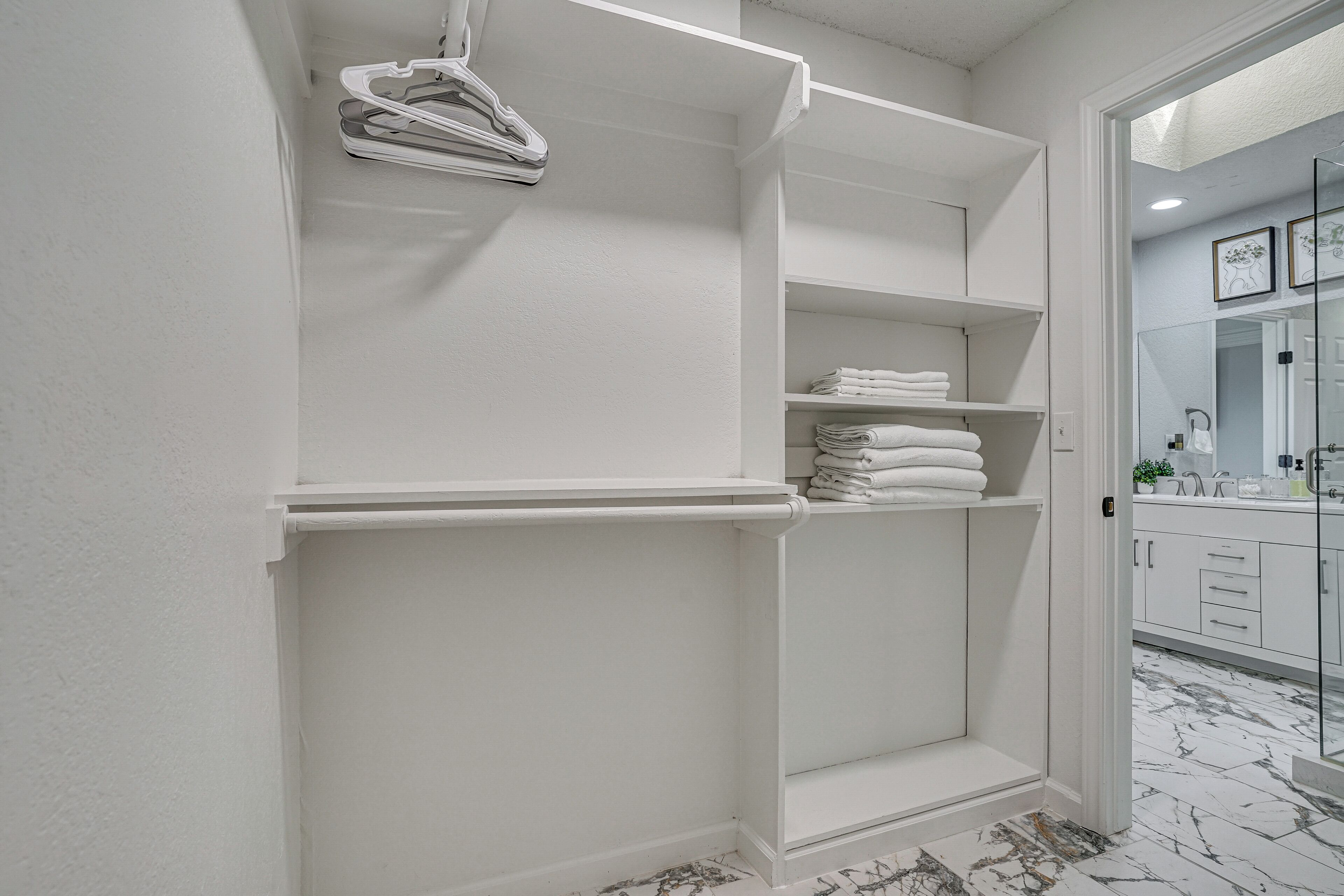 Een witte badkamer met een marmeren vloer, een glazen douchecabine en een witte wastafel met een spiegel.