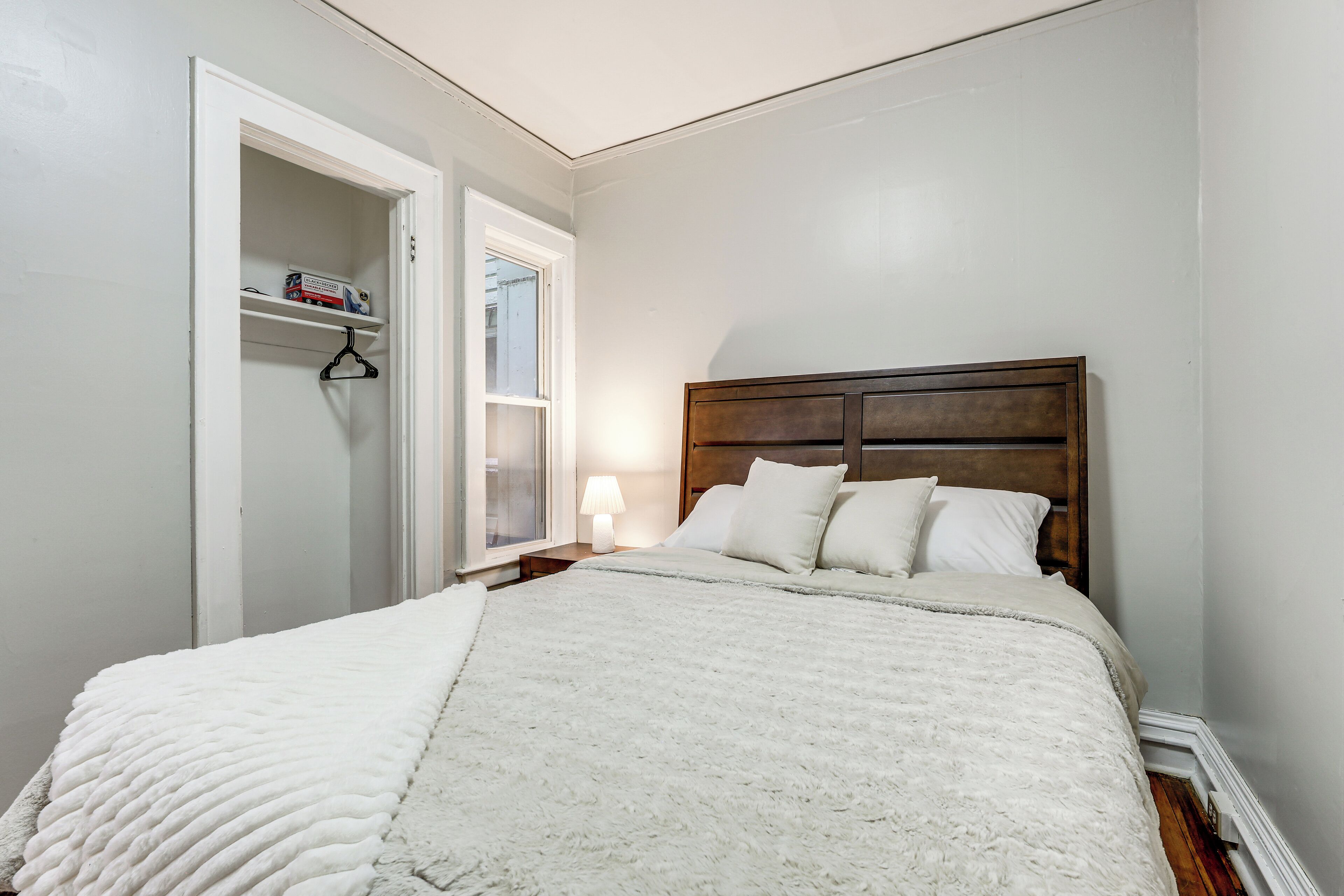 A bedroom with a bed, a nightstand, a lamp, a closet, and a window.