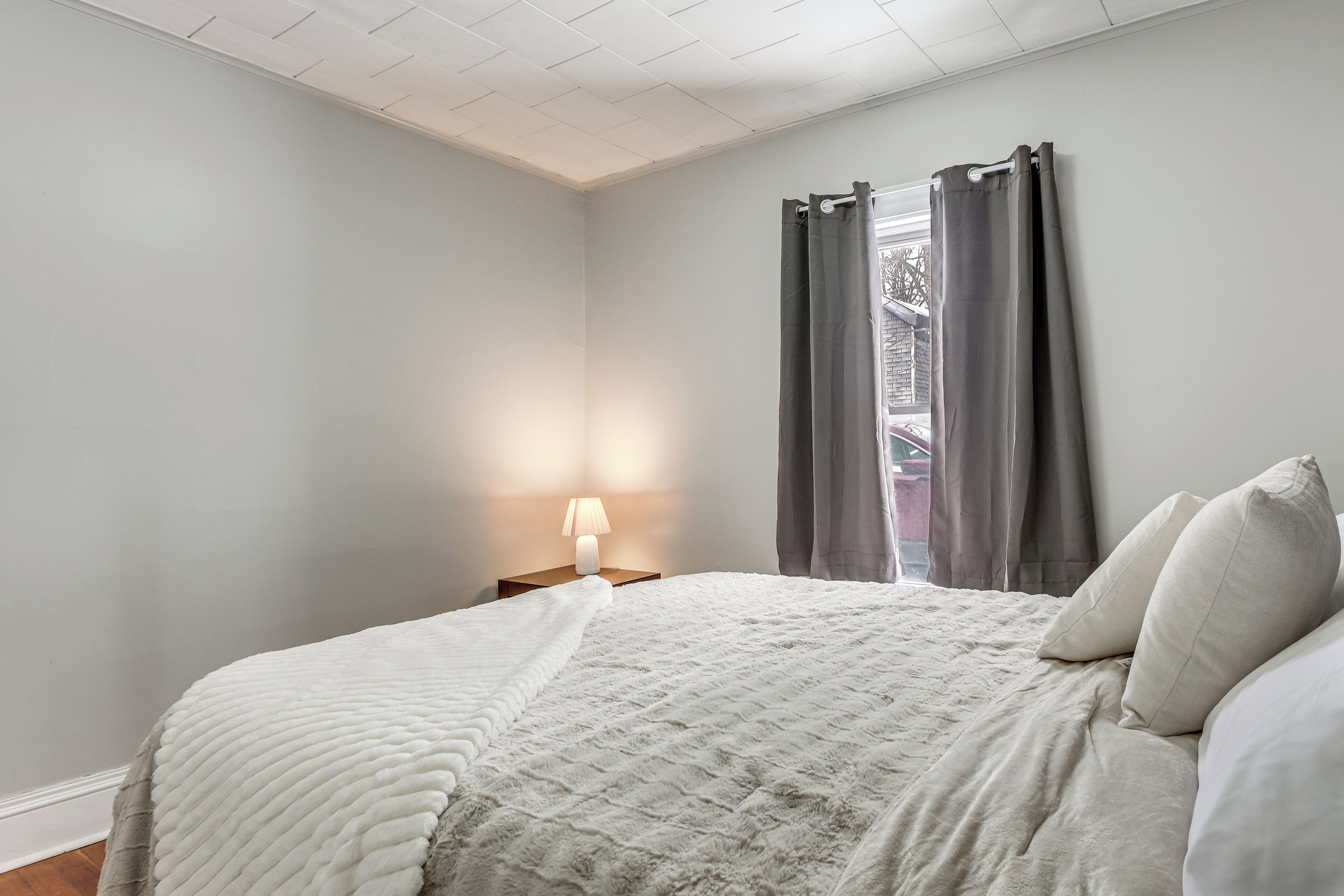 Een slaapkamer met een bed, nachtkastje, lamp en een raam met gordijnen.