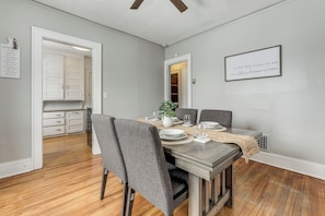 A dining area with a wooden table set for four, grey upholstered chairs, and a kitchen visible through an open doorway. - 8 Mi to Micron Technology! Walkable Phoenix Gem (Phoenix)