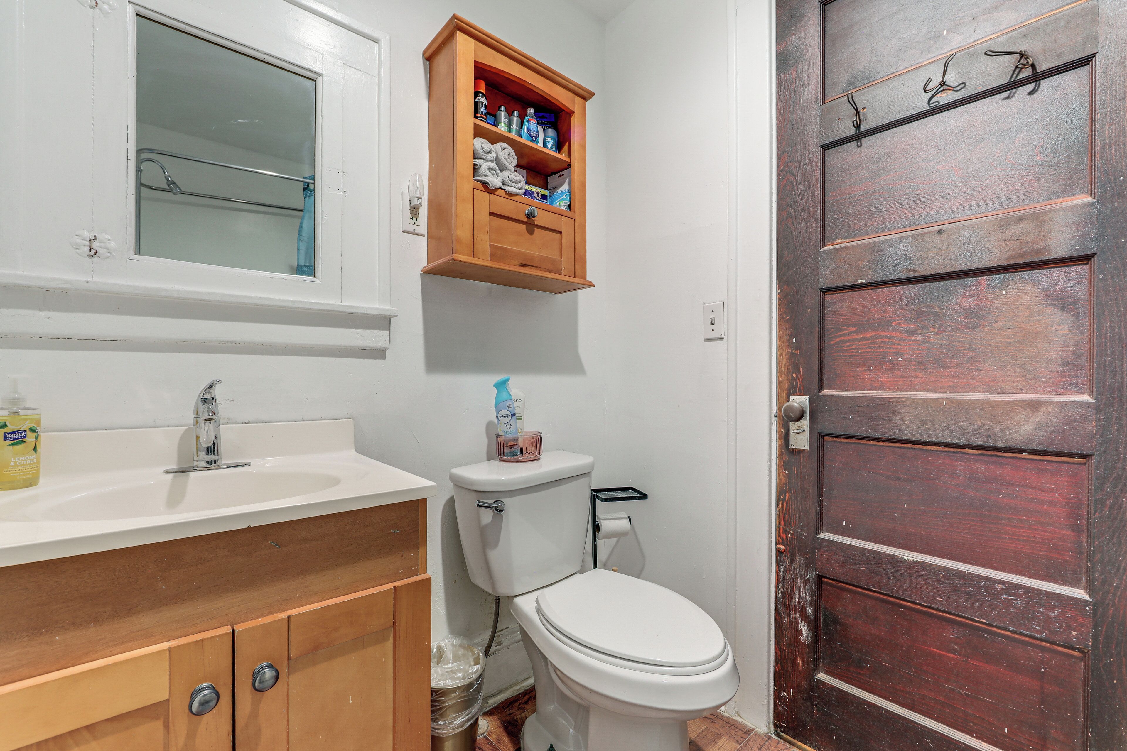 A bathroom with a white sink, wooden cabinets, a mirror, a toilet, and a wooden door.