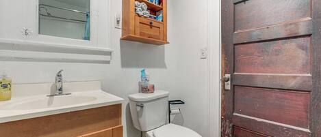 A bathroom with a white sink, wooden cabinets, a mirror, a toilet, and a wooden door.