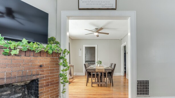 A dining area with a brick fireplace, a ceiling fan, and a sign above the door.