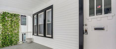 A white exterior with a black-framed window, a door with an American flag sticker, and a white lattice fence.