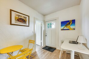 A room with a white door, a yellow table, a white desk with a laptop, and two paintings on the wall.