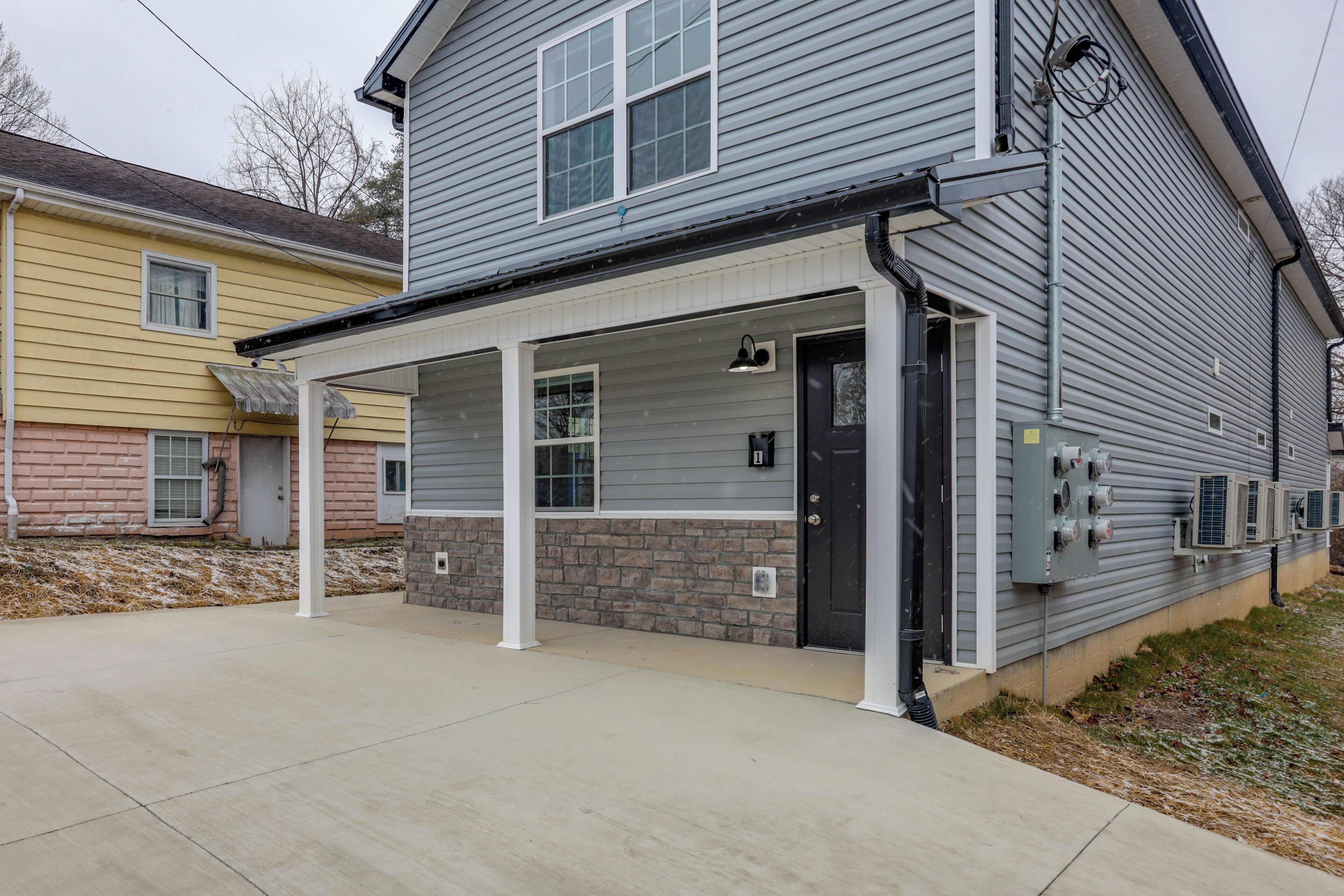 A residential building with a covered porch, brick foundation, and an air conditioning unit on the exterior wall.