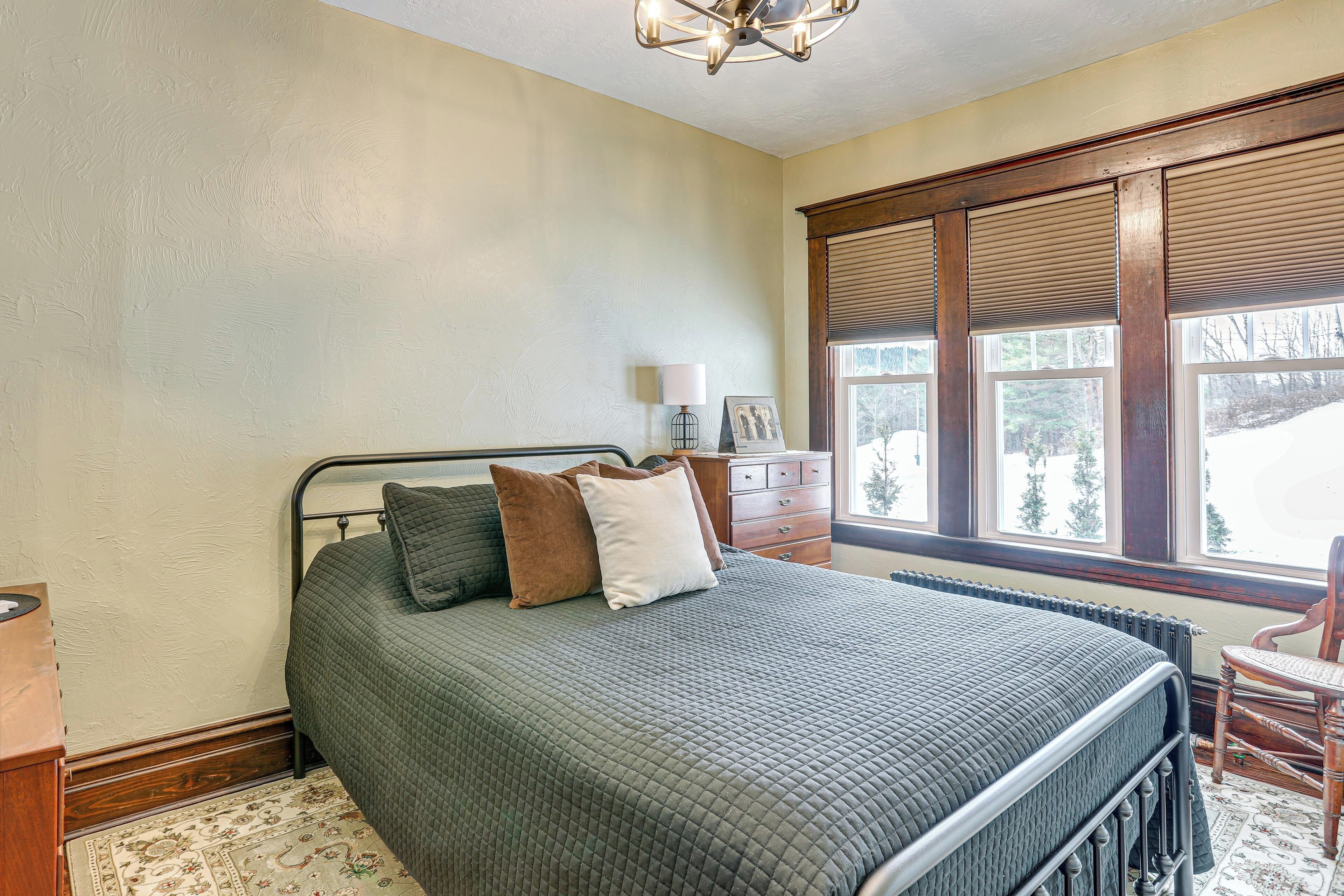 A bedroom with a bed, a nightstand, a dresser, a chair, and a window with blinds.