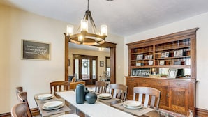 A dining room with a wooden table set for four, surrounded by chairs, a chandelier, and a wooden cabinet with framed photos. - Gateway to PA Wilds: Brockport Family Home! (Brockport)