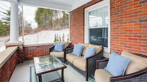 A covered patio with a brick wall, a glass table, and wicker furniture. - Gateway to PA Wilds: Brockport Family Home! (Brockport)