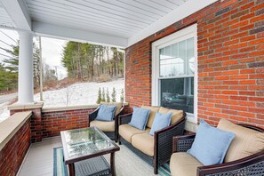 Eine überdachte Terrasse mit Backsteinmauer, Glastisch und Korbmöbeln.