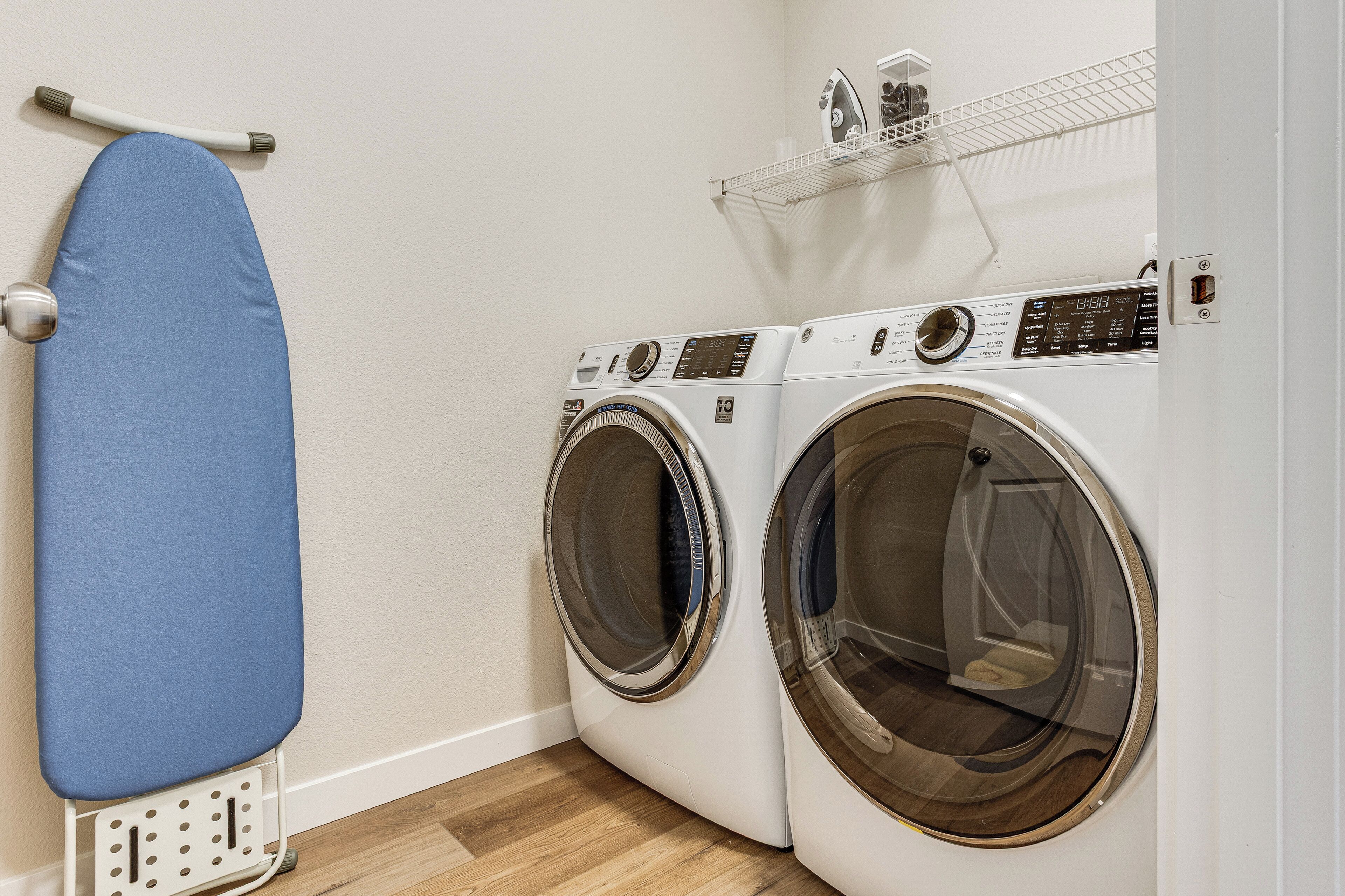 A laundry area with two front-loading washing machines and a blue ironing board.