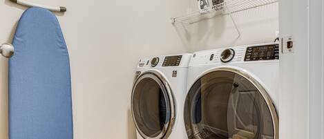 A laundry area with two front-loading washing machines and a blue ironing board.