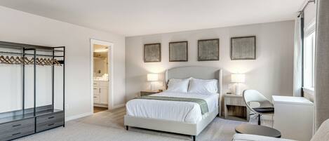 A modern hotel room with a large bed, a desk, a chair, and a wardrobe.