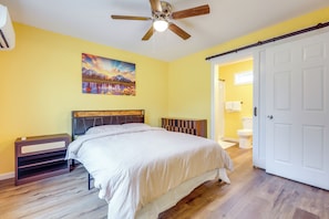 A bedroom with a bed, a ceiling fan, a painting, a nightstand, and a bathroom visible through an open door. - Explore Downtown Ashland! Cozy + New Apartment (Ashland)