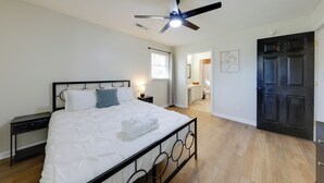 Une chambre à coucher comprenant un lit, des tables de chevet, un ventilateur de plafond et une porte donnant sur une salle de bain.