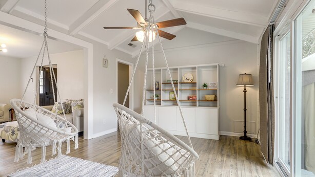 Un salon spacieux doté d’un ventilateur de plafond, de chaises en macramé, d’un plancher en bois et d’une bibliothèque.
