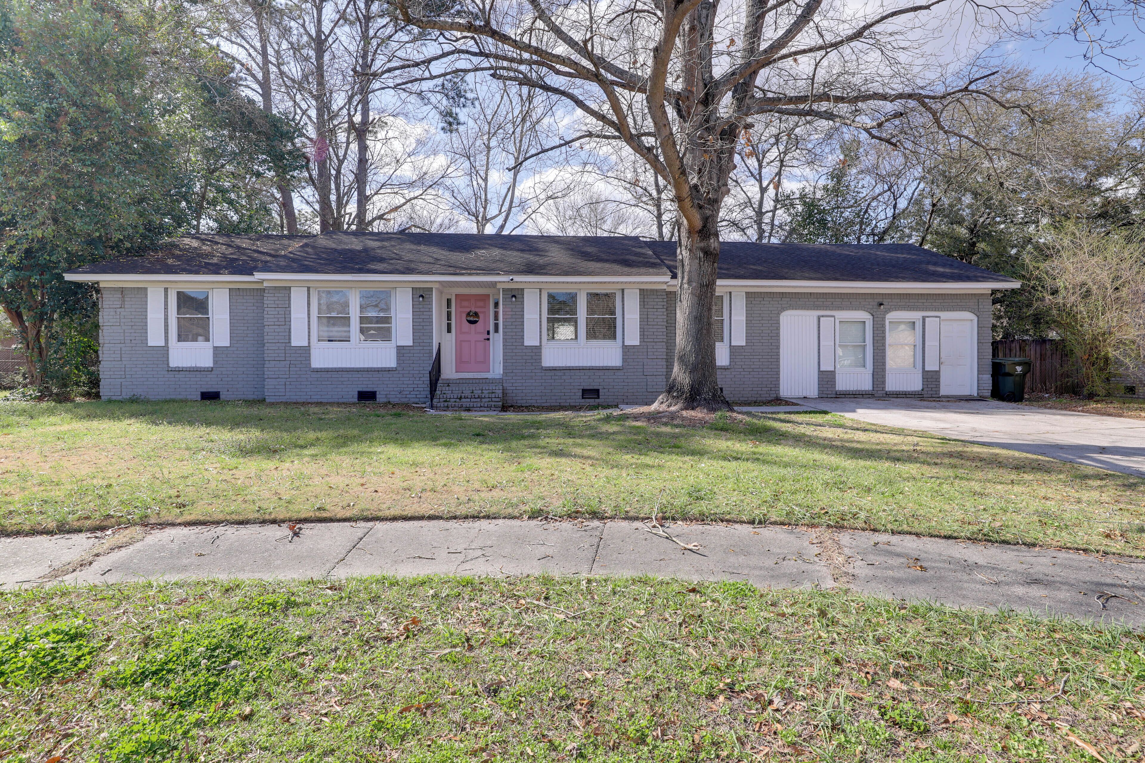 A single-story house with a front porch, a pink door, and a tree in front.