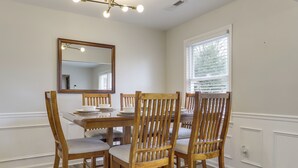 Un coin repas avec une table et des chaises en bois, un miroir et une fenêtre avec des stores.