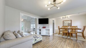 Un salon spacieux avec un canapé, une table à manger et des chaises, un téléviseur fixé au mur et un plancher en bois.