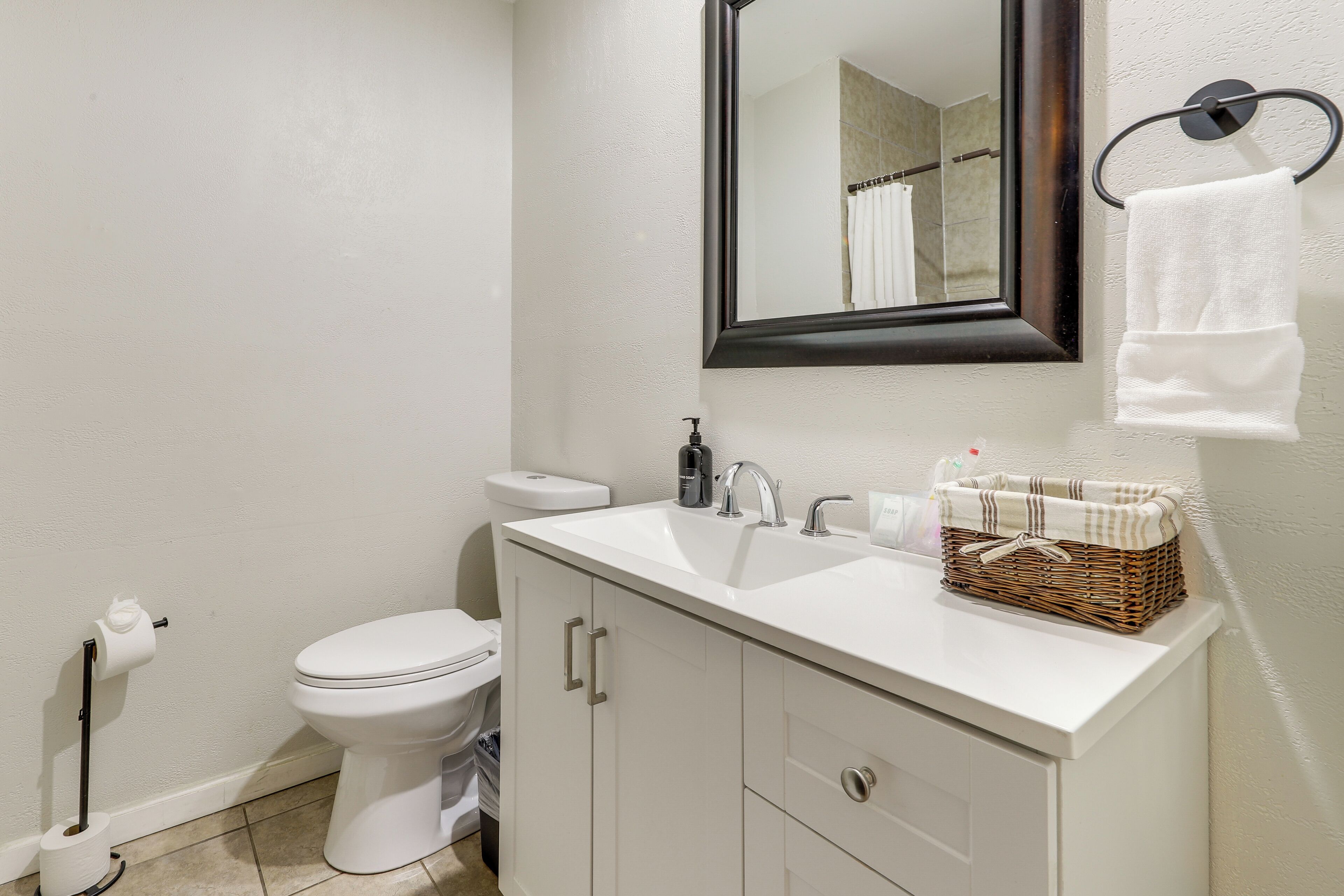 A bathroom with a white sink, a mirror, a toilet, and a wicker basket on the sink.