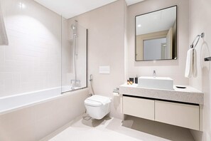 A modern bathroom with a glass shower enclosure, a white toilet, a sink with a mirror above, and a towel rack. - Silkhaus Modern 1bdr Marina Vista Private Beach (Dubai)