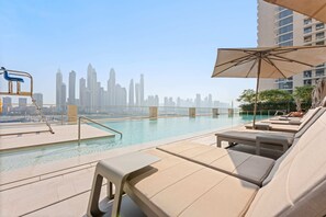 Área de piscina no terraço com espreguiçadeiras e guarda-sol, com vista para o horizonte urbano.