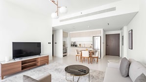 A modern living room with a flat-screen TV, a wooden entertainment unit, a round coffee table, and a sofa. - Silkhaus Modern 1bdr Marina Vista Private Beach (Dubai)