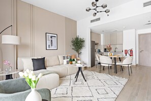 A modern living room with a sofa, a dining table, and a kitchen in the background. - Silkhaus 1bdr in Water s Edge Canal View In Yas (Abu Dhabi)