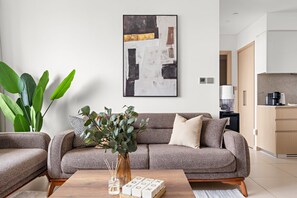 A modern living room with a grey sofa, a coffee table, and a large abstract painting on the wall. - Silkhaus High Floor in Burj Royale Stunning View (Dubai)