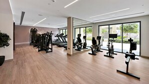 Une salle de sport moderne équipée de divers appareils d’exercice, dotée de grandes fenêtres et d’un plancher en bois.