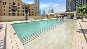 Une piscine sur le toit, agrémentée de chaises longues et de parasols, entourée de gratte-ciel et offrant une vue sur un ciel dégagé.