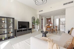 A modern living room with a large flat-screen TV, dark wooden shelving, a beige sofa, and a dining area with a table and chairs. - Silkhaus 1bdr Serene Stay in Reem Island (Abu Dhabi)