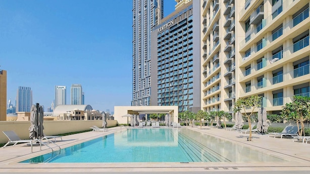 A rooftop swimming pool with lounge chairs and umbrellas, surrounded by high-rise buildings. - Silkhaus Luxurious 1BR Downtown Burj Royale (Dubai)